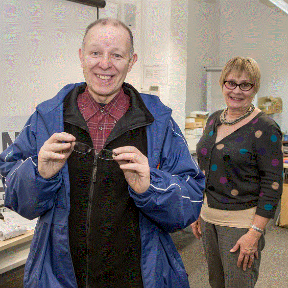 Homeless patient collecting new glasses from volunteer dispensing optician - both smiling